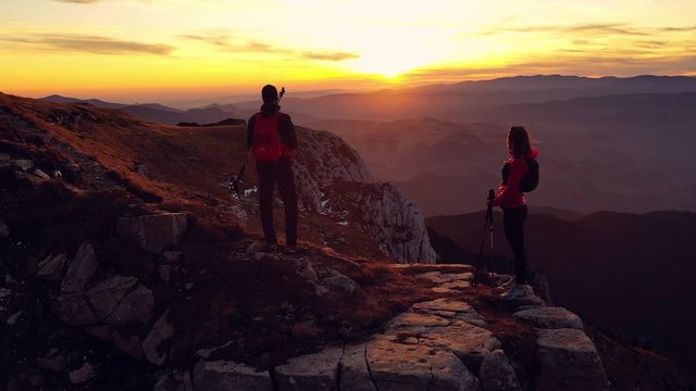 Aerial 4k drone clip with couple of hikers watching a beautiful sunset on top of Bucegi mountain ridge, during magical golden hour light in autumn season, in Romania