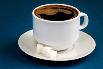 Black coffee espresso in white cup and saucer, blue color background with empty space for text, unhealthy food concept  