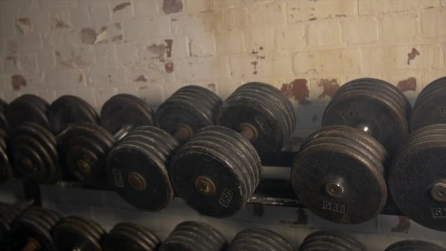 Pan Across Of Weights Lined Up On Weight Rack In Industrial Gym Old Style Old Fashioned Under Ground Gym. Paint Work Scratched Off