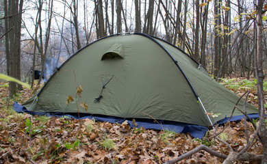 A khaki-colored tent spread out in the forest. Autumn