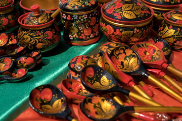 Fototapeta na wymiar Souvenir painted wooden spoons and caskets with floral patterns lie on red with green shiny material.