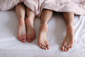 Couple's feet on white sheets under a blanket in hotel selective focus