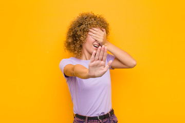 young afro woman covering face with hand and putting other hand up front to stop camera, refusing...
