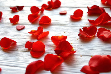 Red rose petals and small red wooden hearts on a white wooden background. Close-up. Side view. St. Valentine's Day background. 