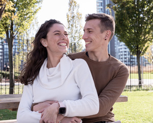 A couple in love millenials hugging each other on a bench and laughing with joy, outdoor couple life, love concept