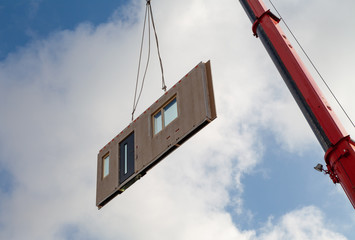 Component for a prefabricated house is transported from an orange jib of a mobile crane for assembly
