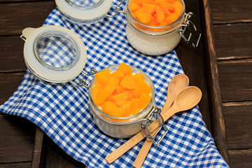 Panna cotta classical italian desert with peaches in two white jar on a brown wooden background on...