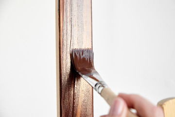 Protective acrylic varnish coating of wooden surface. Wood Finishing. Paintwork. A synthetic paint brush, easel, brown color varnish, female hand of carpenter