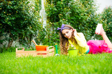 Garden woman with tools. Beautiful girl lie on grass at her spring garden. Young pretty woman enjoy spring nature and take care about her plants. Eco garden worker concept.
