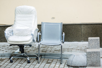 Modern white leather armchair and plastic office chair. New furniture for office left outdoor. Moving to new office