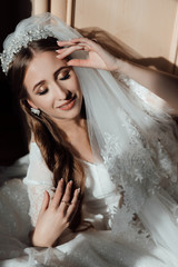 Gorgeous beauty young bride portrait. Beautiful bride with wedding makeup touches the crown. Bridal fashion posing in home. The bride touches the crown. Morning of beautiful bride. Wedding day