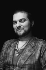 black and white low-key portrait of cheerful confident handsome bearded stylish elegance man in chechered blazer looking at camera on dark background