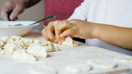 Grandmother with granddaughter is making dumplings with cheese at home kitchen together