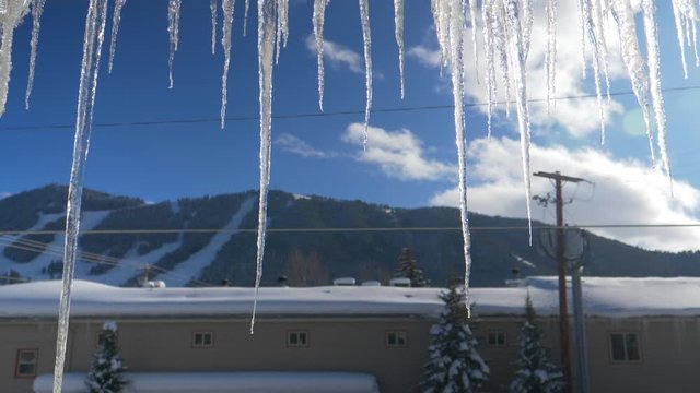 CLOSE UP: Crystal clear ice hangs off the roof of a building with poor insulation. Detailed shot of glassy icycles that have grown on a gutter overnight. Extreme winter conditions in the US mountains.