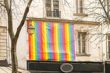 Facade with gay pride flag instead of a window Paris, France. Rainbow flag of the LGBT community as...