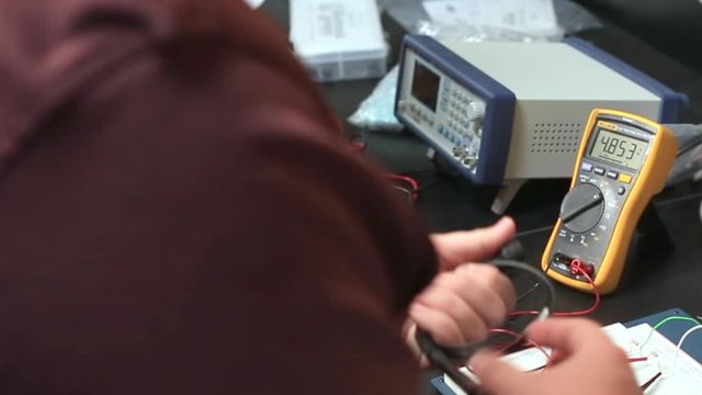 Technology college students learning with electronics engineering voltmeter on work bench.