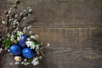 Obraz na płótnie Canvas Blue colored easter eggs in a nest with willow branches and spring flowers on a gray wooden background. Top view flat lay background. Copy space.