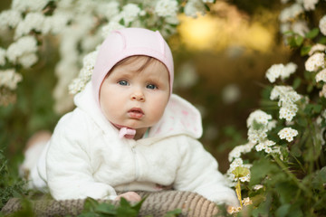 Cute little baby girl in spring in a blooming garden, looking at the camera. Concept: spring, March 8, children. The care for the baby.