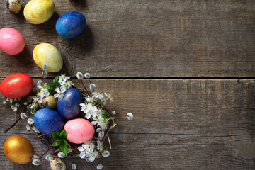 Easter eggs in a nest with willow branches and spring flowers on a gray wooden background. Top view flat lay background. Copy space.