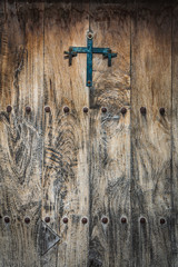 Antique wooden door decorated with a cast iron cross and iron studs