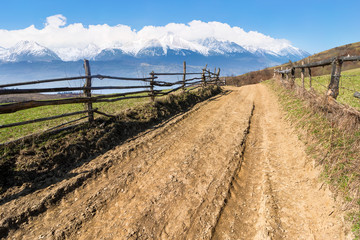 Fototapeta na wymiar rural landscape in spring. composite landscape of mountain ridge in the distance with snow capped tops and fields with fence along the country dirt road. warm sunny weather