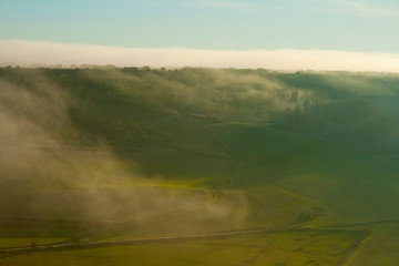 Green fields in a valley with fog falling at sunset.