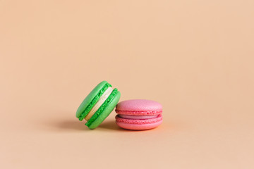 Two tasty french macarons on peach pastel background.  Pink and green macarons.