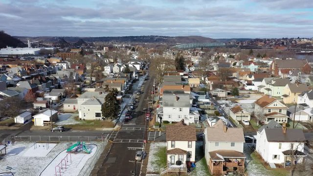 A slow forward moving winter aerial establishing shot of the city of Monaca, Pennsylvania, a small rust belt town. Factories and bridges on the Ohio River, in the distance. Pittsburgh suburbs.  	