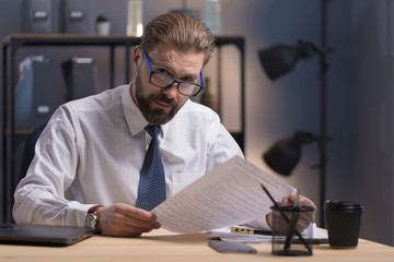 Portrait of mature company CEO at work, looking at camera over his glasses