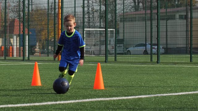 Preteen boy and girl practicing football skills while dribbling balls around cones standing in lines on sports field and trying to score goal. Young active soccer players during training on playground