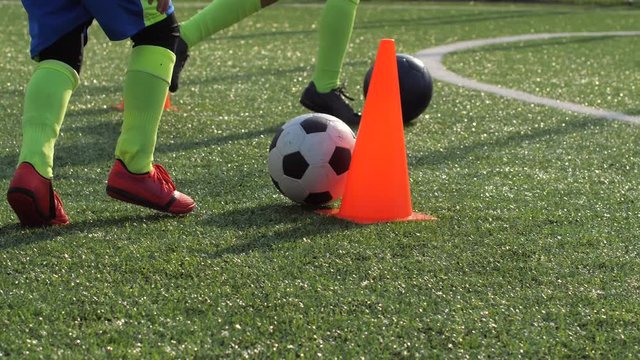 Close-up of kid's legs developing football skills on sports ground with artificial grass. Young soccer players learning to dribble balls past cones and score goals during training on football field