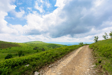 Fototapeta na wymiar mountain dirt road scenery. path through the grassy meadows on rolling hills. ridge in the distance. green carpathian landscape. cloudy summer weather. dramatic sky