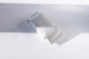 Blank foil food or drink bag on white background in minimal style, natural light shadow. Monochrome...