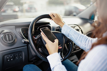 Portrait of a young woman texting on her smartphone while driving a car. Side view of young woman holding blank screen cell phone while driving car. Don't text and drive concept