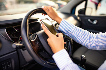 Young woman holding blank screen cell phone, driving car. Female business woman driver hand on steering wheel & checking smartphone in moving vehicle. Don't text and drive concept. Close up,background