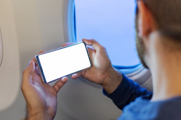 Mockup smartphone airplane. Young attractive european man holding blank screen smartphone in hands in airplane. Mock up for a game, mobile application, web site a horizontal oriental. Stock photo.