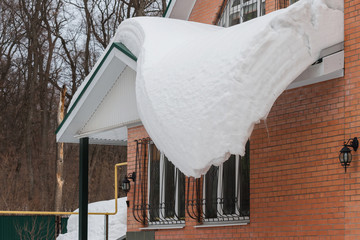 A large layer of snow slowly slides from the roof of the house, it is dangerous