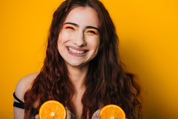 Beautiful girl on a bright yellow background. Model with fruit in hand. Two orange slices. Broad smile