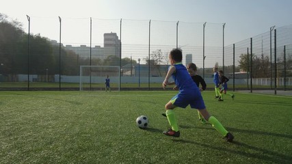 Young forward taking pass, masterfully bypassing back player and scoring goal during football match between children's teams. Active preteen footballer showing good skill while playing soccer outdoors - Powered by Adobe