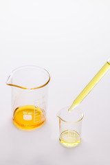 two beakers with orange and yellow liquids standing, a glass pipette full of yellow oil, small home laboratory