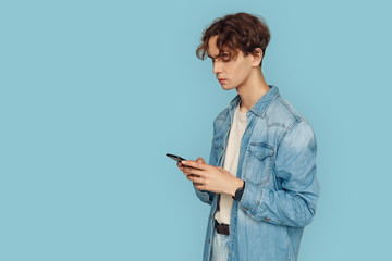 Freestyle. Man in denim shirt standing isolated on gray chatting on smartphone concentrated