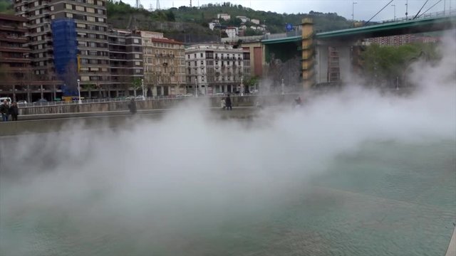 Full shot, People walking  on the side of  foggy river in Bilbao, Spain, next to Gugenheim museum.