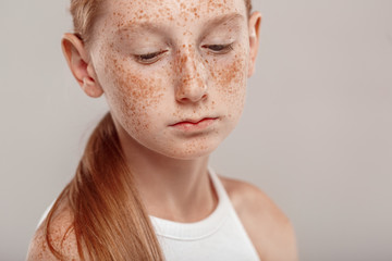 Inclusive Beauty. Girl with freckles standing isolated on grey looking down upset close-up