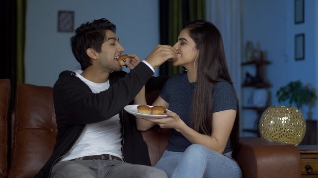 Cute Indian couple in love feeding muffins to each other on valentine's day in India. Young boyfriend girlfriend happily spending quality time together while having freshly baked fruit muffins on t...
