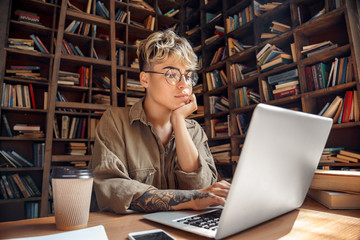 Distance Education. Young woman short hair in glasses sitting at desk studying online on laptop...