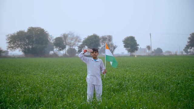 Young village boy salutes with Indian National flag - Republic / Independence day. Cute little kid in traditional kurta pajama showing his patriotism while saluting the tricolor flag of India with ...
