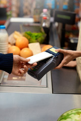 Daily Shopping. Man standing at the supermarket cashier counter paying for purchases with smartphone contactless close-up