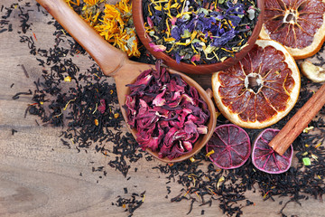 Assortment of dry tea. different varieties of tea on a wooden table. blended tea with flower petals, hibiscus in a wooden spoon and dried citruses. top view. - obrazy, fototapety, plakaty