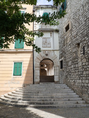 Fototapeta na wymiar Rincón con una fachada de piedra un arco en la entrada y escaleras en Sibenik, Croacia, verano de 2019