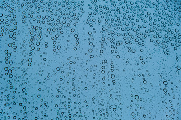 Raindrops on Transparent Glass Surface on a Cold Snowy Winter Background